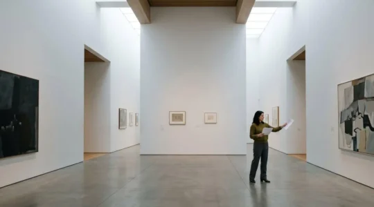 A curator reviewing exhibition layout plans in a contemporary museum gallery with artworks in background